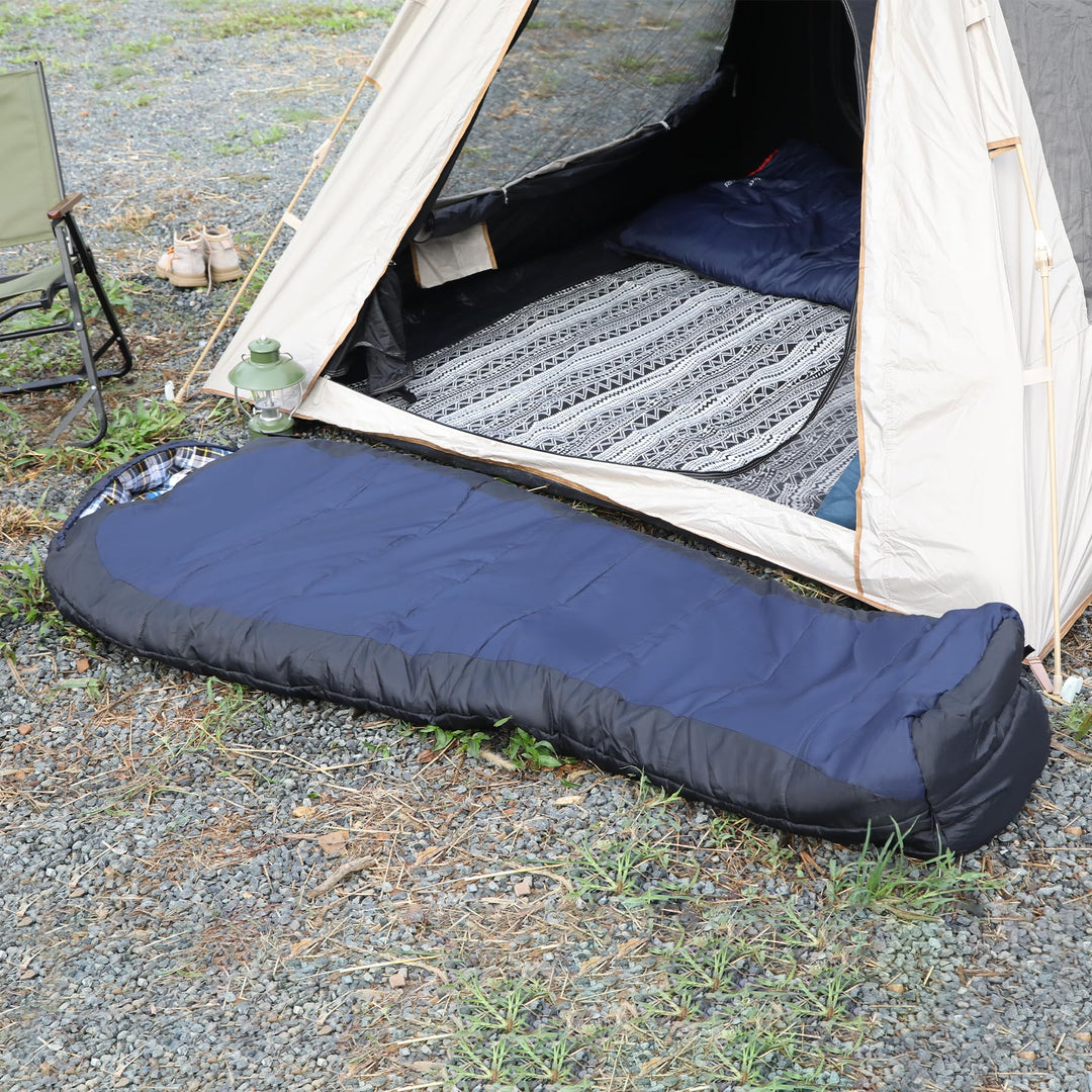 Navy mummy sleeping bag laid out beside a camping tent